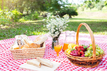 Fototapeta na wymiar Healthy food and accessories outdoor summer or spring picnic, Picnic wicker basket with fresh fruit, bread and a glass of refreshing orange juice in the camping nature background