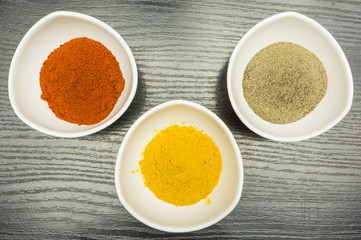 On the kitchen table, a set of three bowls with spices - pepper, paprika and curry.View from above.