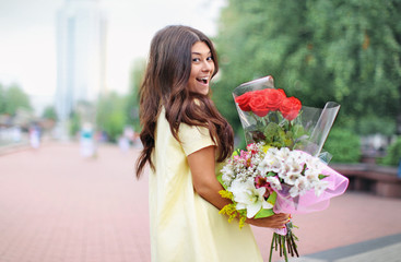 the young beautiful girl has a birthday and she is happy standing with a bouquet of flowers and smiling at the background of the city park