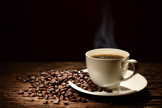 Cup of coffee with smoke and coffee beans on black background © amenic181