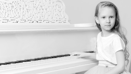 A little girl is sitting at the white piano.