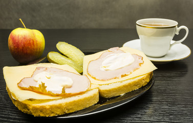 A plate with sandwiches with ham, cheese and mayonnaise, and a cucumber. An apple and a cup of tea.