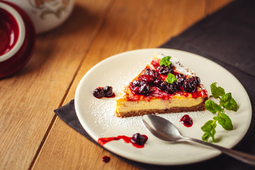 Beautiful traditional italian cheesecake with red fruits, mint, and powdered sugar on wooden background, selective focus