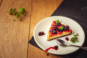 Beautiful traditional italian cheesecake with red fruits, mint, and powdered sugar on wooden background, selective focus