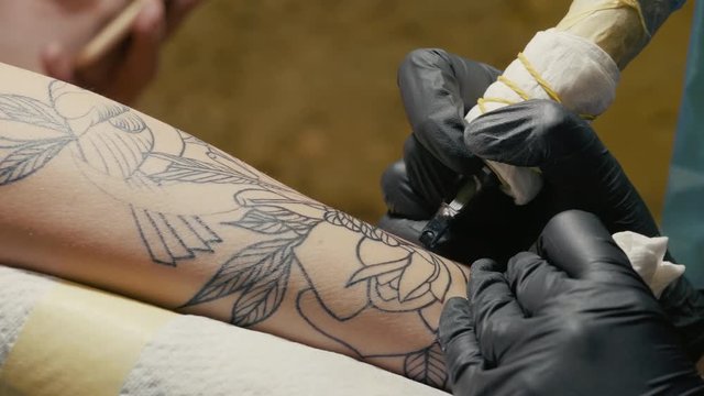 Macro view of professional tattoo master is painting with black ink, making shadow. Works in black latex gloves with handmade rotor gun machine in studio. 4k