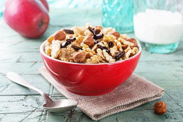Corn flakes with hazelnuts and chocolate  in red bowl for breakfast on old cyan wooden table