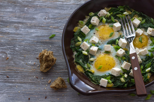 Green shakshuka with spinach, leek and feta in a ceramic frying pan on a wooden table with bread, free space, selective focus. Delicious healthy home food
