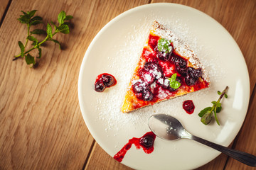 Beautiful traditional italian cheesecake with red fruits, mint, and powdered sugar on wooden background, selective focus