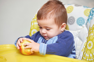 Baby boy in the baby chair with apple
