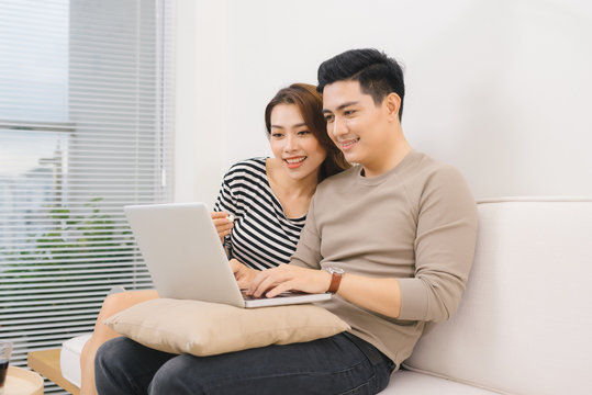 Happy Asian Couple In Love Surfing On Laptop At Home