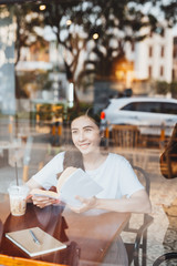Asian woman reading book vintage color tone. Viewed through window of cafe.