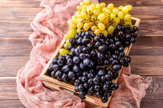 Photo of black grapes in wooden box with pink cloth