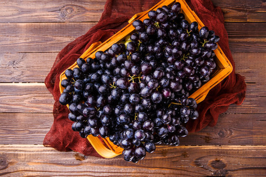 Image from above of black grapes in wooden basket with claret cloth