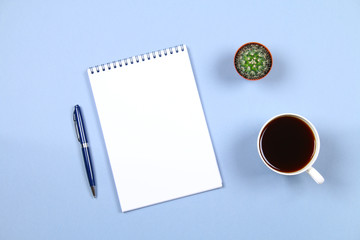 Empty notebook with pen, coffee and cactus on a blue background. Copy the space. Top view.