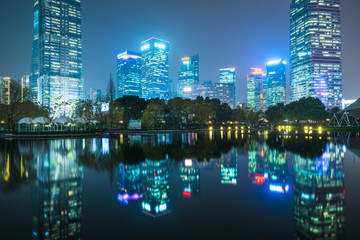 illuminated modern skyscrapers standing by park lake at night,shanghai,china.