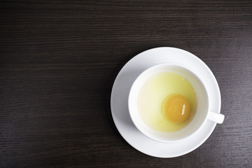 Fresh egg in white cup on wood background.