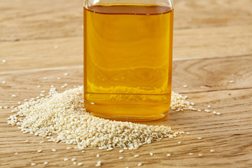 Peeled sesame seeds with oil in a small bottle over wooden background, close-up, shallow depth of field, selective focus