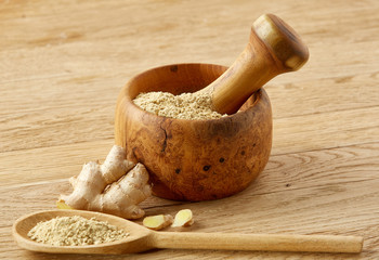 Wooden mortar and pestle with ginger and grind spices on rustic table, close-up, selective focus