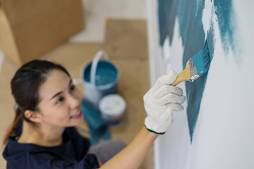 Young asian couple painting interior wall with paint brush
