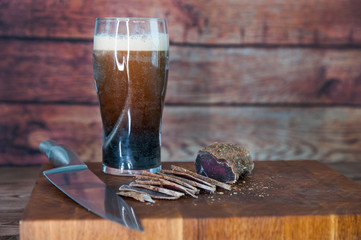 Portion of Beef Jerky cutting into slice on a cutting table with dark beer glass and a kitchen...