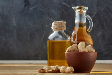 Fototapeta na wymiar Aromatic oil in a glass jar and bottle with peanuts in bowl on wooden table, close-up