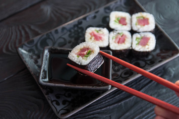 Hand using chopsticks pick. Maki-Sushi, tuna-maki rolls in front of face of young man. Fresh made Sushi set with tuna, cheese and cucumber. Traditional Japanese cuisine.
