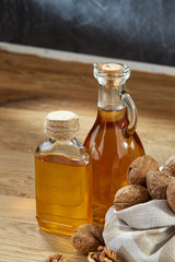 Aromatic oil in a glass jar and bottle with peanuts in bowl on wooden table, close-up, vertical