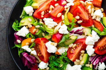 Vegetable dish, salad with avocado, pepper, tomato, italian mix, fresh lettuce, feta cheese and pine nuts. Healthy food. Top view