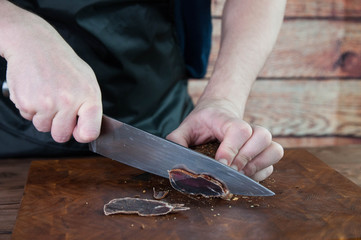 Portion of Beef Jerky cutting into slice on a cutting table with dark beer glass and a kitchen knife on vintage wooden background, man standing behind