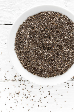 Chia seeds in bowl on white wooden background. Top view
