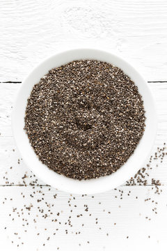 Chia seeds in bowl on white wooden background. Top view