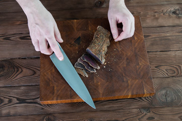 Portion of Beef Jerky cutting into slice on a cutting table with a kitchen knife on vintage wooden...