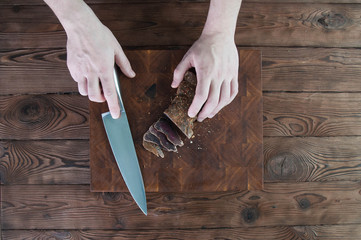 Portion of Beef Jerky cutting into slice on a cutting table with a kitchen knife on vintage wooden background
