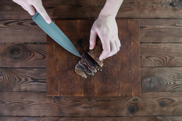 Portion of Beef Jerky cutting into slice on a cutting table with a kitchen knife on vintage wooden...