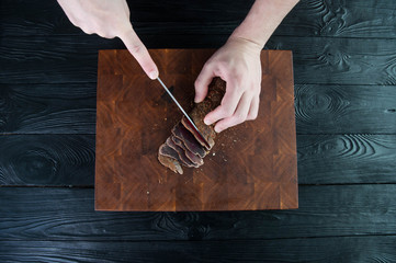 Portion of Beef Jerky cutting into slice on a cutting table with a kitchen knife on vintage wooden...