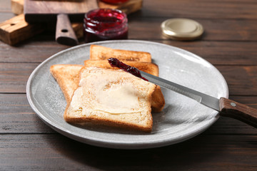 Plate with tasty toasted bread, butter and jam on table