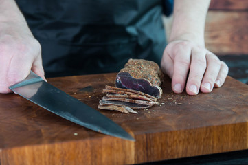 Portion of Beef Jerky cutting into slice on a cutting table with a kitchen knife on vintage wooden...