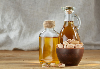 Aromatic oil in a glass jar and bottle with pistachios in bowl on wooden table, close-up.