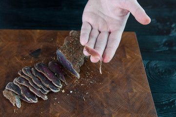 Portion of Beef Jerky cutting into slice on a cutting table with a kitchen knife on vintage wooden...