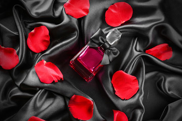 Bottle of perfume and rose petals on black silk