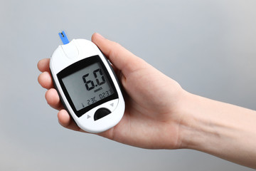 Woman holding digital glucometer on light background. Diabetes concept