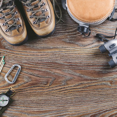 Hiking or travel equipment with boots, compass, binoculars, flask on wooden background. Active lifestyle concept.