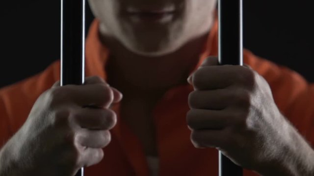 Cruel serial killer holding jail cell bars, prisoner hands closeup, law breaking