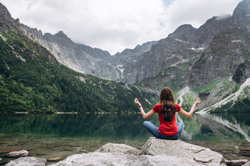 Fototapeta premium Young fitness woman meditating on the shore of the mountain lake