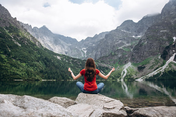 Young fitness woman meditating on the shore of the mountain lake