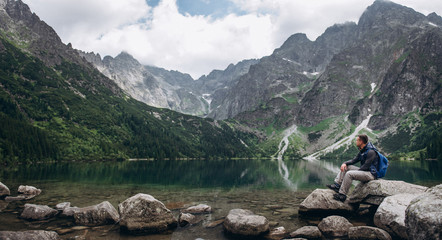 The man sitting on a rock on the shore of a mountain lake enjoys a landscape