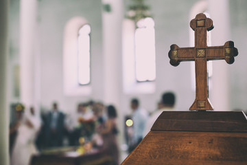 Wedding event in a church the old wooden cross is in a first view and the people are blurred in the...