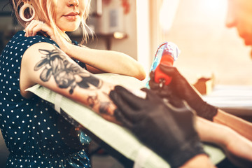 Young beautiful girl looks like the tattoo artist does the tattoo, reading the news in the...