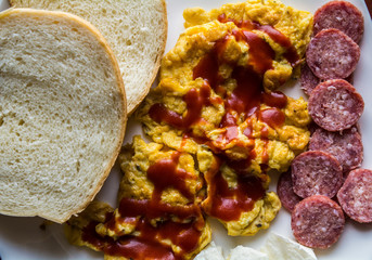 Scrambled eggs with ketchup with bread, salami  and cheese