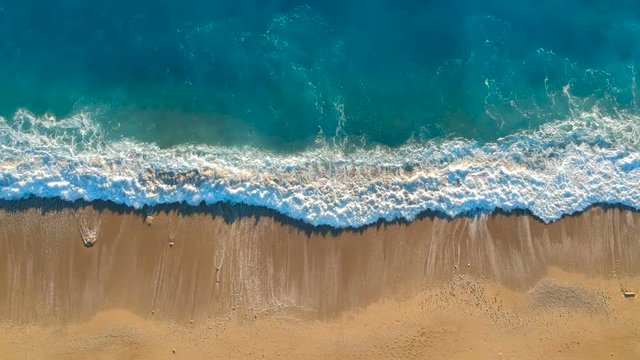 Aerial view looking straight down onto crashing waves hitting a golden beach